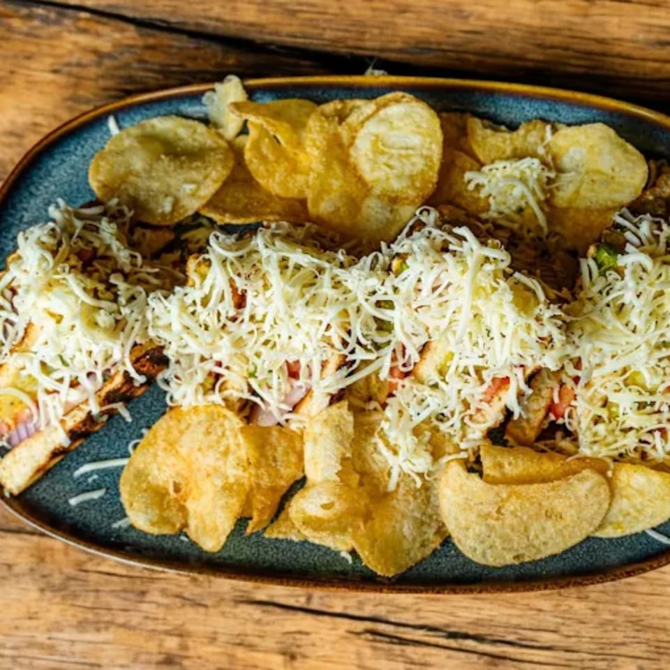 Indian-style bruschetta topped with shredded cheese and served with crispy potato chips on a blue plate.