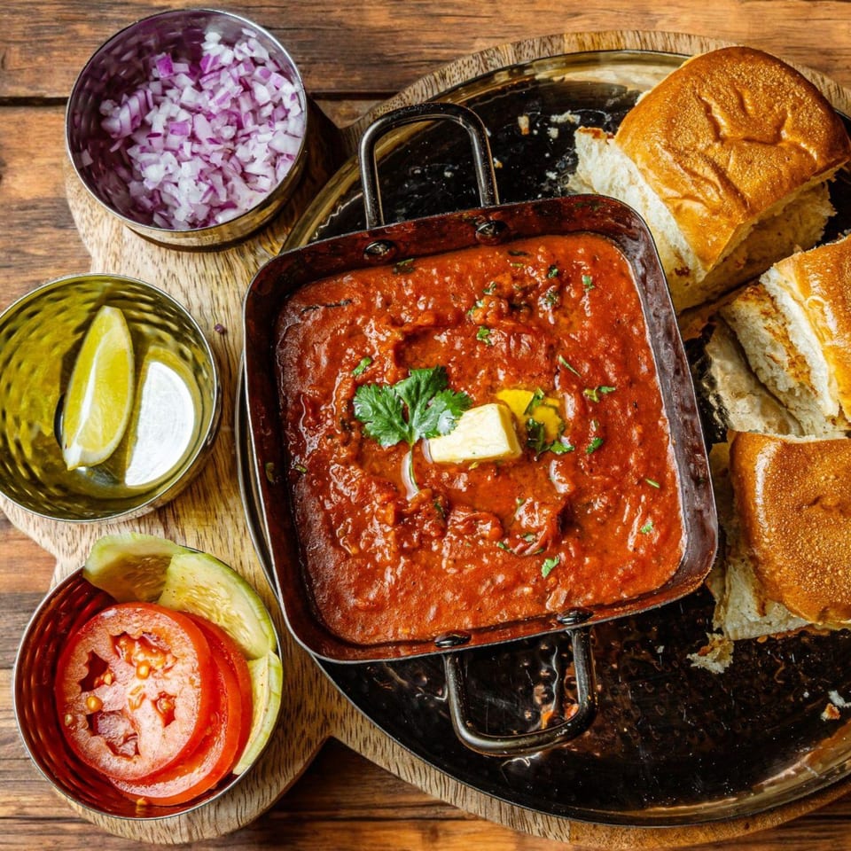 Mirch Masala Town's Pav Bhaji, a vibrant red curry with butter, served with bread, onions, lime, and tomatoes.