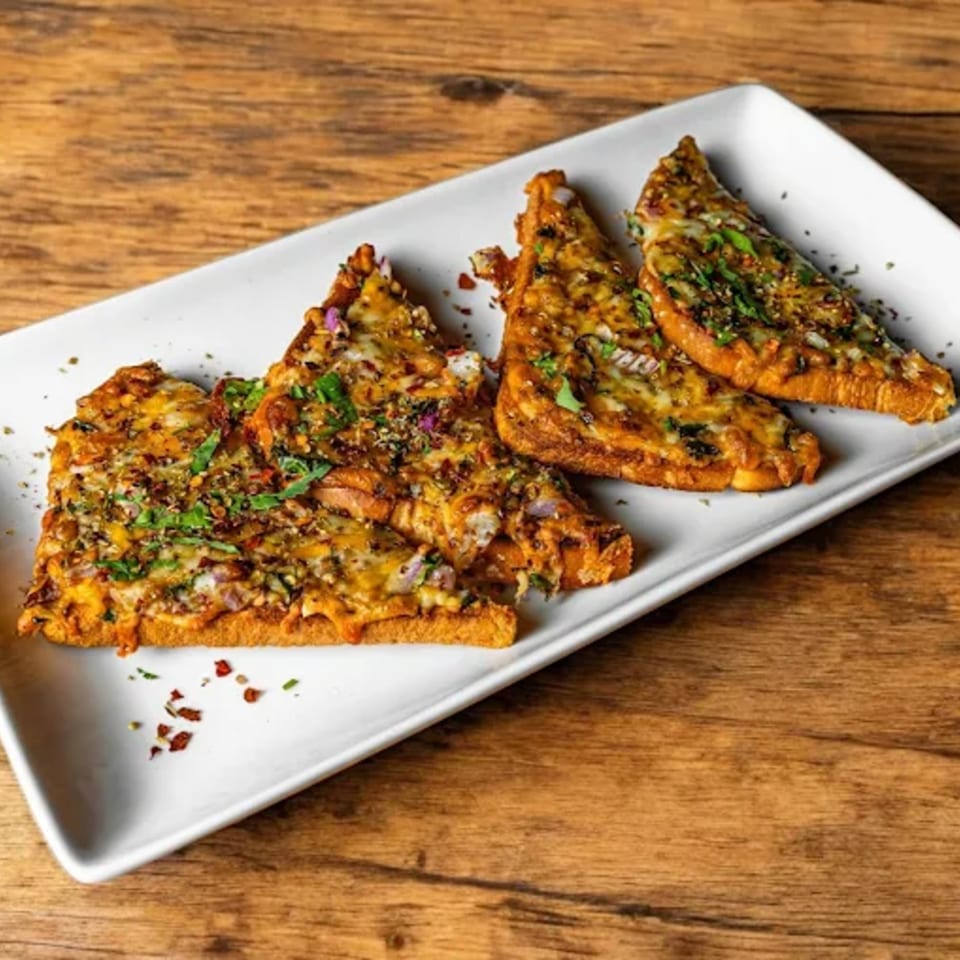 Four pieces of Indian chili cheese toast, garnished with herbs, on a white rectangular plate.