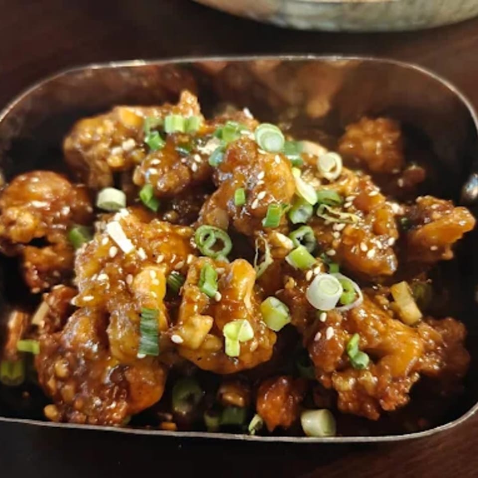 Mirch Masala Town's Indian-style chili chicken, garnished with sesame seeds and green onions in a metal bowl.