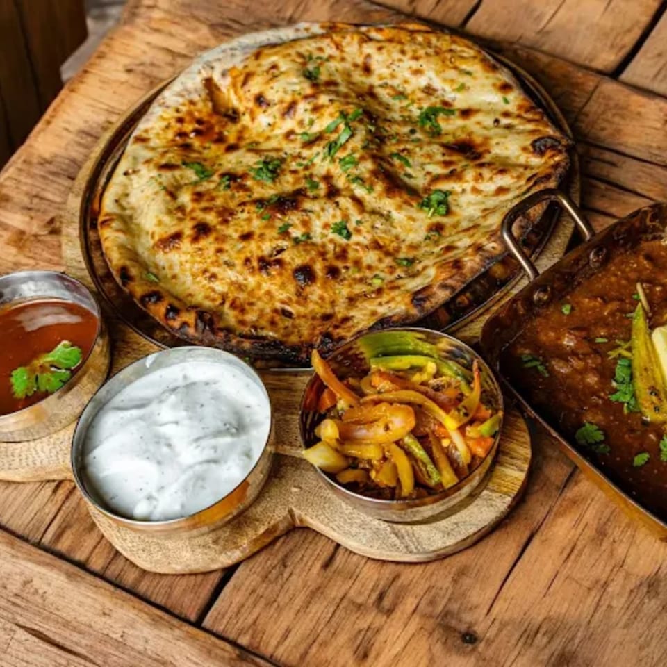 Indian naan bread, curry, and side dishes on a rustic wooden table at Mirch Masala Town.