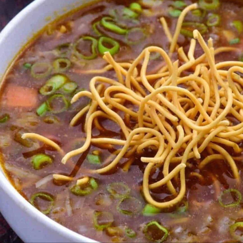 Close-up of Mirch Masala Town's Indian soup with noodles, green onions, and vegetables.